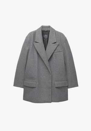 Harmaa villasekoitteinen takki, jossa on viisto kaulus, jämäkät olkapäät, kaksi etutaskua ja yksi rintatasku. Takissa on rento istuvuus.