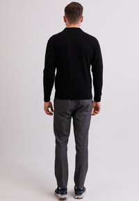 Mustat neuleet, jossa on pyöreä kaula-aukko, yhdistetty harmaisiin ruutuhousuihin. Jalkineet ovat tummansiniset lenkkarit, joissa on valkoiset pohjat.