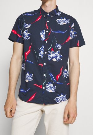 Chemise bleue marine à manches courtes ornée d'un motif floral en blanc, rouge et bleu, avec un col boutonné et en tissu de coton lisse.