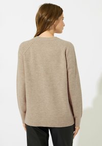 Beżowy sweter z mieszanki wełny o luźnym kroju, z rękawami raglanowymi i ściągaczem na dole. Posiada jednolitą kolorystykę z delikatną teksturą.
