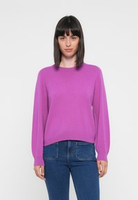 Lilla strikkegenser med rund hals, lange ermer og en avslappet passform. Kombinert med blå denimjeans, som har en klassisk femlommersdesign.