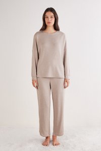 Beige loungewear set bestaande uit een top met lange mouwen, een ronde halslijn en een comfortabele pasvorm, gecombineerd met bijpassende broek met wijde pijpen. Zachte textuur.
