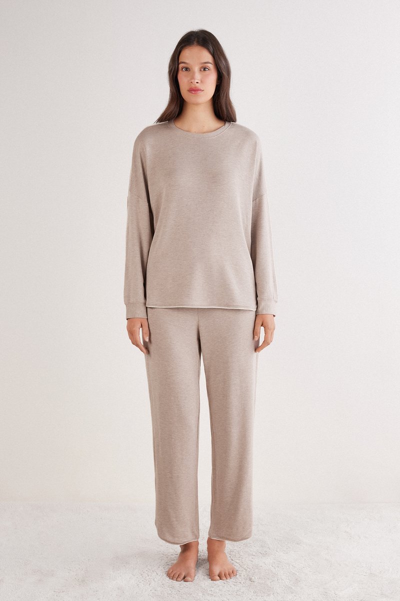 Beige loungewear set bestaande uit een top met lange mouwen, een ronde halslijn en een comfortabele pasvorm, gecombineerd met bijpassende broek met wijde pijpen. Zachte textuur.