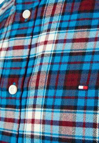 Blauwe, rode en zwarte geruite shirt met een knoopsluiting, textuurstof, witte knopen en een klein merklogo in rood, wit en blauw.