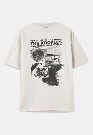 Camiseta de manga corta color crema con un gran estampado gráfico negro que incluye texto e imágenes, cuello redondo y ajuste relajado. Detalle de dobladillo deshilachado.