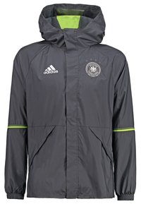 Giacca a vento Adidas grigia con fodera verde, dotata di zip frontale, cappuccio regolabile e logo con emblema sul petto.