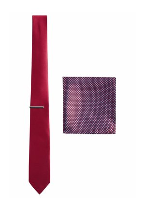 Red tie with a textured surface alongside a square pocket square featuring a navy background and small blue and red diamond patterns.