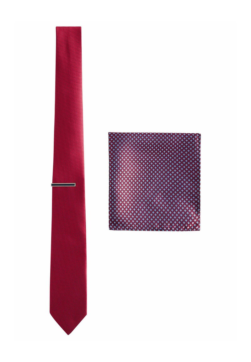 Rote Krawatte mit strukturierter Oberfläche neben einem quadratischen Taschentuch mit Navy-Hintergrund und kleinen blauen und roten Diamantmustern.