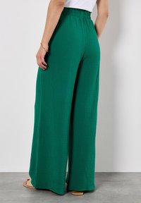 Wijde groene broek van textuurstof met een gathering en elastische tailleband. Het ontwerp heeft een ontspannen pasvorm en een vloeiende silhouet.