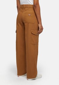 Brown wide-leg cargo pants with multiple pockets, made of durable cotton material. Features a logo patch on the back waistband.