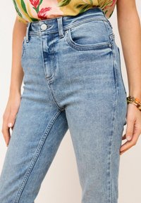 Světle modré džíny vyrobené z denimu, s vysokým pasem, pěti kapsami a kovovým zapínáním, s jemným vyblednutím na látce.