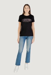 T-shirt nera in cotone con una grafica scintillante in argento e rosa. Abbinata a jeans azzurri e sneakers bianche.