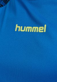 Blå sportskjorta i slätt material med en stor gul "hummel"-logotyp tydligt synlig på framsidan.
