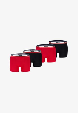 Muskolöser männlicher Oberkörper, der rote Levi's Boxershorts mit weißem und marineblauem Bund trägt, steht vor einem schlichten hellen Hintergrund.
