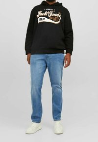 Felpa nera con grafica e testo bianco e arancione, abbinata a jeans in denim azzurro chiaro e sneakers bianche. Look casual e vestibilità rilassata.