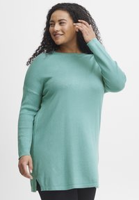 Maglione lungo a maniche con una vestibilità rilassata, colore turchese chiaro, con fessure laterali e texture a coste. Tessuto morbido con scollatura rotonda.