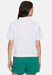 Vit kortärmad polo med krage, med avslappnad passform och lätt uppvikt ärm, matchad med gröna shorts.