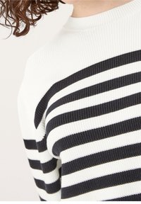 Pull en maille rayé noir et blanc avec une texture côtelée. Présente de larges rayures horizontales et un col montant.