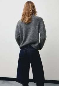 Pull gris duveteux assorti à un pantalon culotte en denim foncé avec une taille haute et une jambe large. L'ensemble présente une silhouette décontractée.