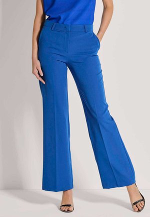 Pantalons larges bleus avec une texture lisse, dotés d'un devant plat, de poches latérales et d'une coupe ajustée. Associés à des talons ouverts noirs.