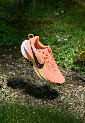 Lightweight running shoe in peach, featuring a breathable mesh upper, black swoosh, and responsive white midsole. Accents include a pull tab.