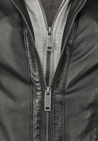Schwarze Lederjacke mit doppeltem Reißverschluss, sichtbar grauem Baumwollfutter und glatter, strukturierter Oberfläche mit detaillierter Nähte.