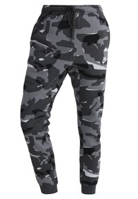 Grå camouflage-mjukisbyxor med dragsko i midjan, ribbade muddar och Nike-logotyp på låret. Tillverkade av mjukt material med varierande nyanser av grått.