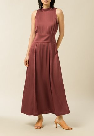 Robe maxi en satin bordeaux avec un col haut, un corsage ajusté et une jupe fluide. Le modèle l'a associée à des mules à talons ouverts beige.