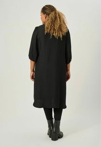 Svart klänning i knälång längd med texturerad tyg, trekvartsärmar och avslappnad passform. Matchad med svarta ankelskängor.