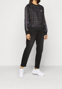 Mikina s černým a červeným mřížkovaným vzorem, černé kalhoty a bílé tenisky. Mikina má žebrované manžety a logo na hrudi.