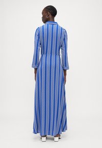 Blaues langärmliges Kleid mit einem weißen Zickzackmuster, Kragen und schwingendem Design, das an den Knöcheln endet und leicht ausstellt.