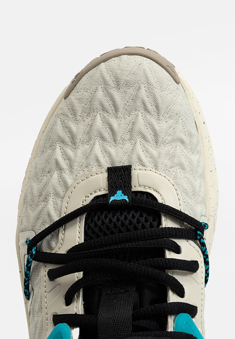 Zapatilla gris claro con parte superior sintética texturizada, lengüeta de malla negra, acentos turquesa en los cordones y suela de goma beige.