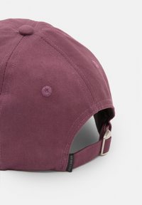 Casquette de baseball en tissu bordeaux avec une surface texturée, une sangle ajustable à l'arrière et une petite étiquette logo sur le côté.