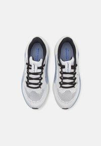 Balto un gaiši zili Nike skriešanas apavi ar melnu šņorēm, skatīti no augšas uz vienkārša baltā fona.