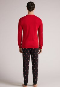 Camiseta roja de manga larga con cuello redondo, combinada con pantalones de pijama negros con un patrón disperso en rojo y blanco. Tejido suave, diseño ajustado.