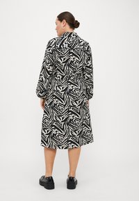 Black and white dress featuring a zebra stripe pattern, long sleeves, a collar, and a tie waist. Worn with black platform shoes.