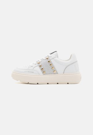 Biały sneaker z grubą podeszwą, srebrzystym brokatowym panelem bocznym i złotymi nitami w kształcie serca. Oznaczenie "Love Moschino" blisko palców.