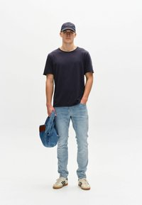 Mornarska majica, svetlo modri džinsi, beli patiki s črnimi črtami in denim jakna. Model drži jakno čez ramo na belem ozadju.