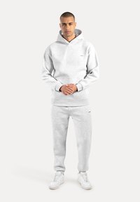 Ljusgrå sweatshirt och matchande sweatpants i mjukt tyg, med huva, kenguruficka och logodetalj. Vita sneakers.