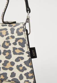 Sac en imprimé léopard avec un bord noir, doté d'un clip argenté, d'une surface texturée et d'une petite étiquette noire.