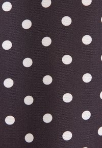 Tissu sombre avec des pois blancs régulièrement espacés dans un motif régulier, montrant une surface tissée texturée.