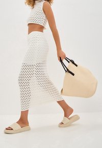 Hvid strikket crop-top og lang nederdel med åbent prikmønster; beige platform sandaler; oversized beige tekstureret tote-bag med sorte håndtag.