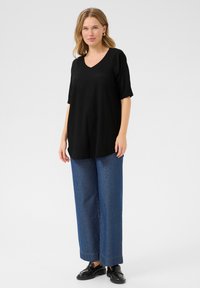 Top nero a maniche corte e scollo a V in tessuto testurizzato, abbinato a jeans blu a gamba larga e mocassini neri. Design semplice e informale.