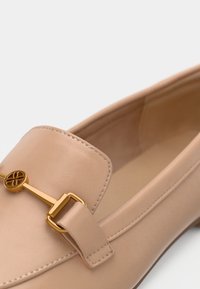 Mocassin en cuir beige avec boucle en métal doré et d étail de sangle, présentant une texture lisse et un bout arrondi.