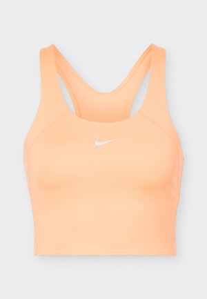 Nike športová podprsenka broskyňovej farby s dizajnom racerback a bielym logom Nike Swoosh uprostred vpredu.