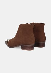Botines de ante marrón con un tacón bajo y apilado, y un diseño de punta con rayas. Cierre lateral para facilitar el calzado. Textura suave y forma clásica.