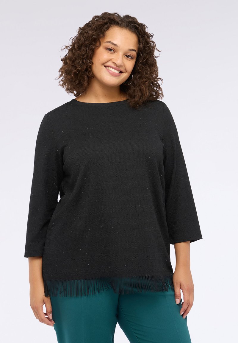 Schwarzes Oberteil mit 3/4-Ärmeln, aus strukturiertem Stoff und fransigem Saum. Das Design umfasst dezente Glitzerakzente für zusätzliche Details.