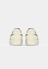 Nike sneakers i creme med en tekstureret læderfinish. Har mørke striber og et fremtrædende logo prægede på hælen. Sålen er designet til godt greb.