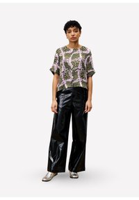 Korte mouw top met een groen, roze en paarse abstracte print, gecombineerd met hoge zwarte vinylbroek en zilveren loafers.