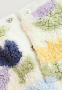 Barevný patchworkový textil s texturovanými chomáči modré, zelené, fialové a žluté vlny, s kovovými patentkami a květinovými knoflíky.